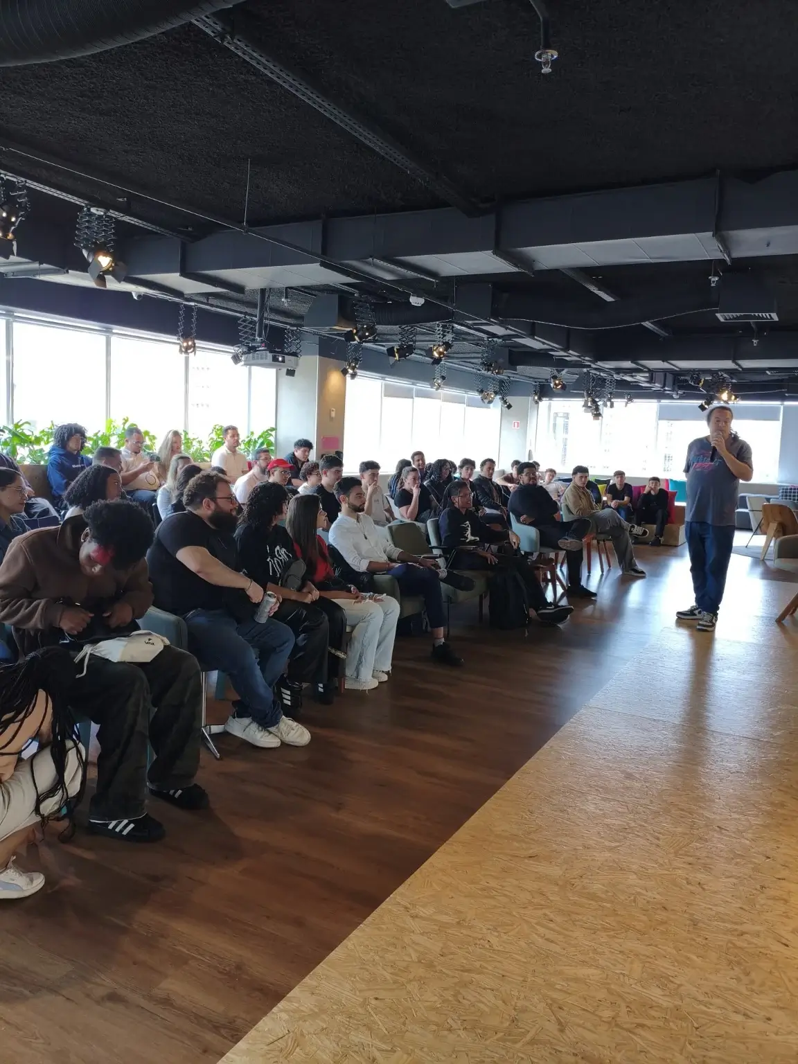 Público sentado ouvindo uma fala num espaço de coworking